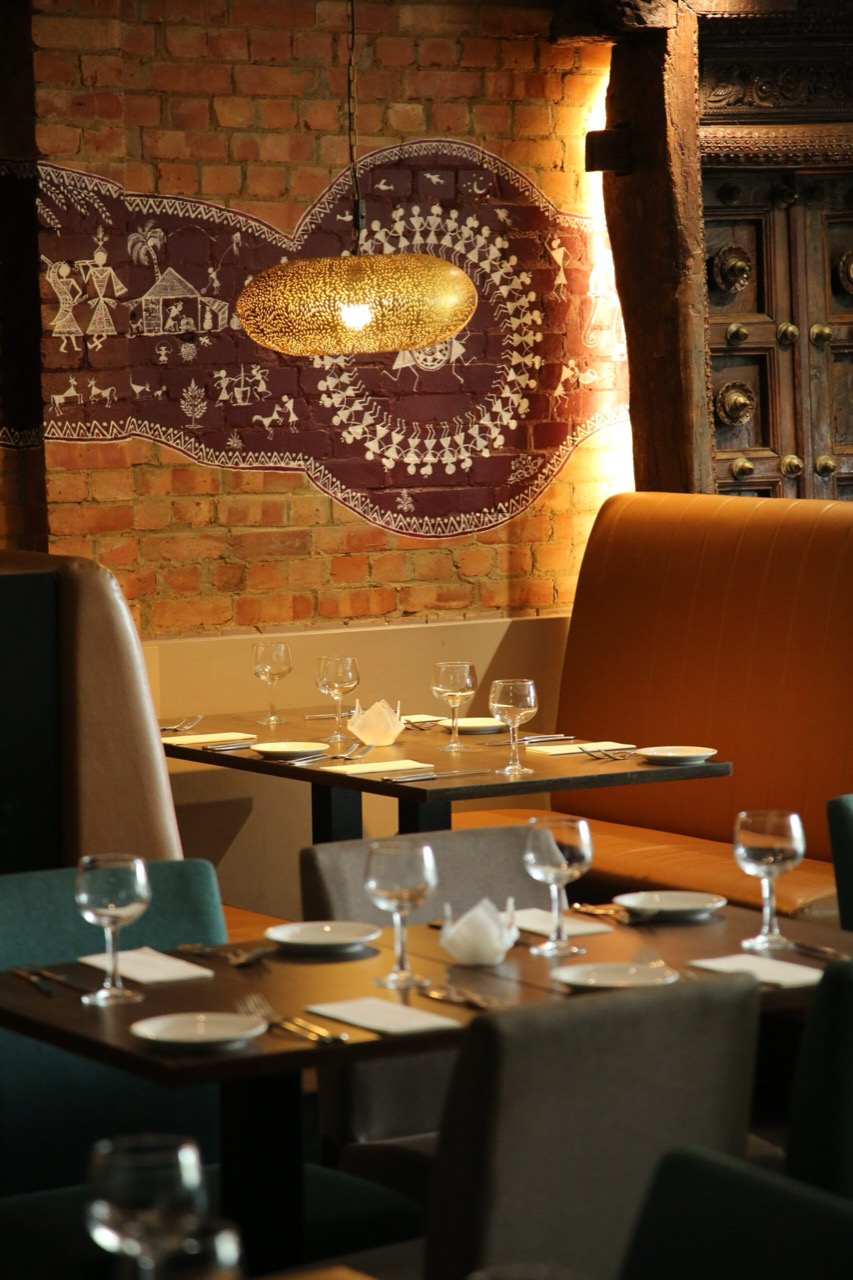 The dining room at Spices and Spirits, laid tables against a brick wall under a brass lamp
